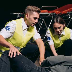 Two individuals in yellow vests provide aid to a man on the ground, showcasing to help in an emergency.