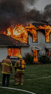 Firefighters in protective gear stand before a burning house, battling the intense flames