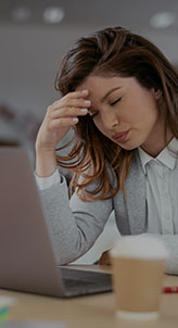 A woman seated at a desk, intensely focused on her laptop, with an expression of stress