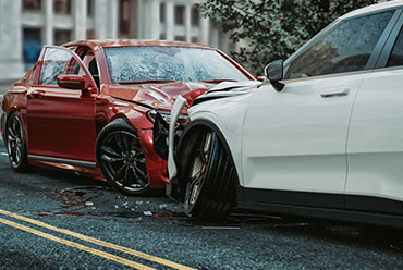 Two cars collided in a car accident. The red car has significant front-end damage, while the white car has damage to its side.