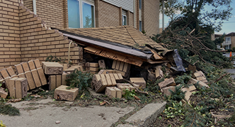 A damaged brick building with a collapsed portion of the roof. Debris, including bricks and wood, is scattered on the ground.