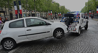 A white car being towed by a tow truck on a cobblestone street.