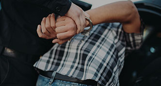 A police officer handcuffing a person. The person is wearing a plaid shirt and jeans.