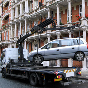 Tow truck lifting a silver car in front of a building symbolizing illegal towing - Charles Injury Law